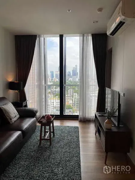 Condominium for rent or sale - Bright living room with floor-to-ceiling window, city view, leather sofa and TV console.
