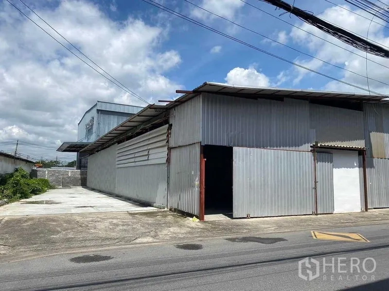 Warehouse for rent in Saphan Sung, Bangkok - Corrugated metal warehouse exterior with large sliding door and wide concrete driveway for loading and parking.