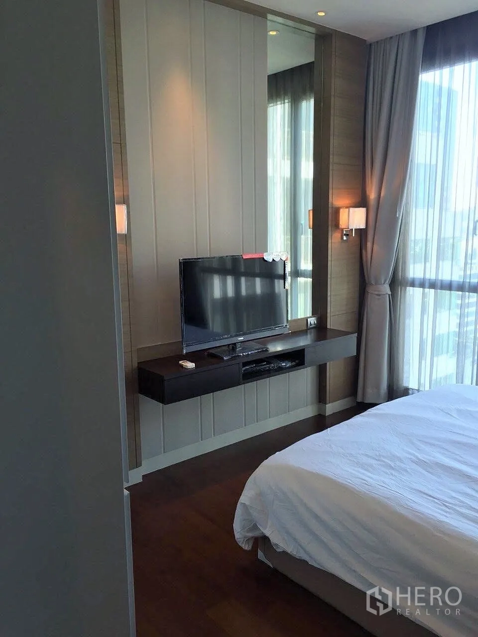 公寓 出租在Watthana, Bangkok - 卧室配大窗与白色床品，壁挂电视与悬浮搁板。