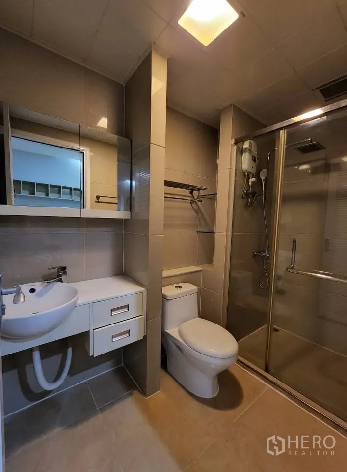 Condominium for rent in Huai Khwang, Bangkok - Tiled bathroom with glass-enclosed shower, water heater, vanity and toilet.