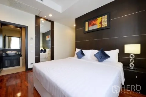 Apartment for rent in Watthana, Bangkok - Master bedroom with dark accent wall, bedside lamps, and en-suite bathroom entrance.