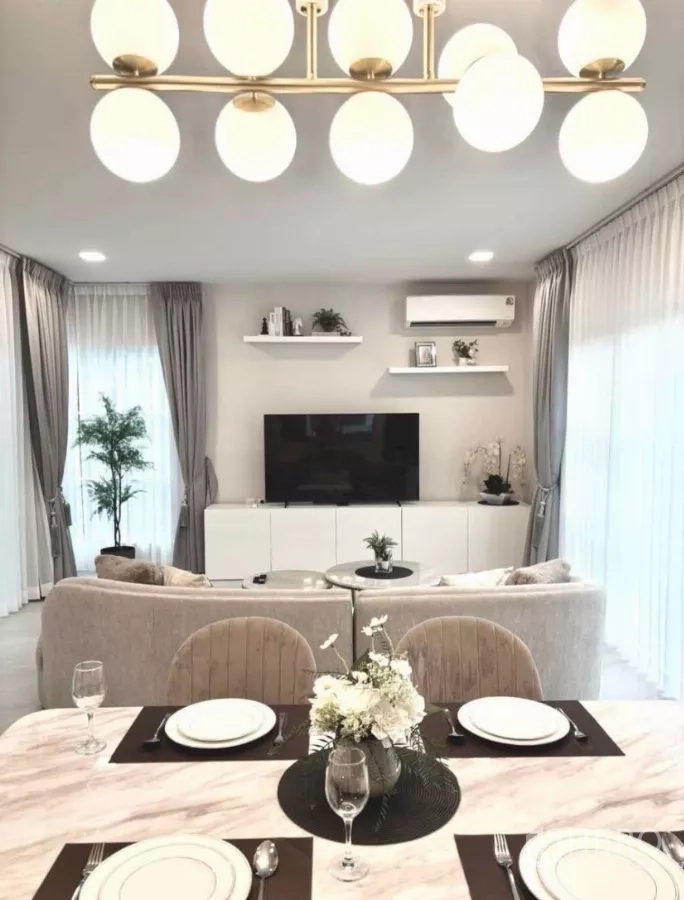 Detached House for rent in Bang Phli, Samut Prakan - Dining table facing a TV wall with a pendant chandelier and sheer curtains.