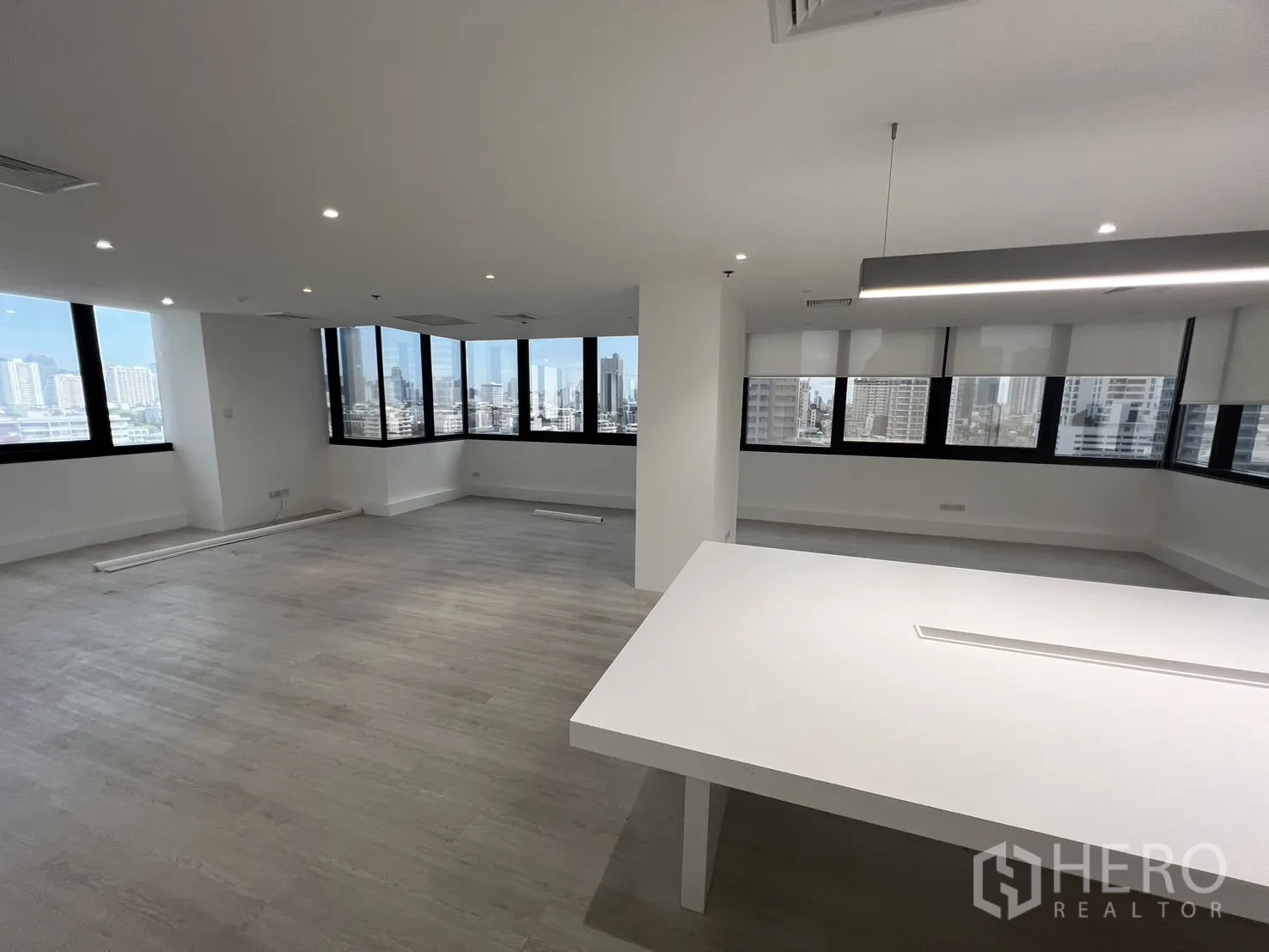 Office Space for rent in Khlong Toei, Bangkok - Open workspace with corner panoramic windows and a hanging linear light above the central table.