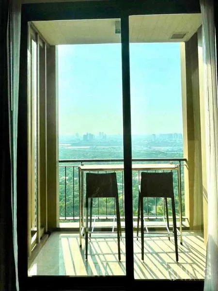 Condominium for rent in Bangkok - Private balcony with high chairs overlooking green city views and skyline.