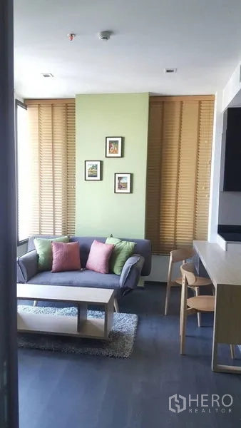 Condominium for rent in Watthana, Bangkok - Cozy living area with sofa and cushions, coffee table, wooden blinds and artwork near the breakfast bar.