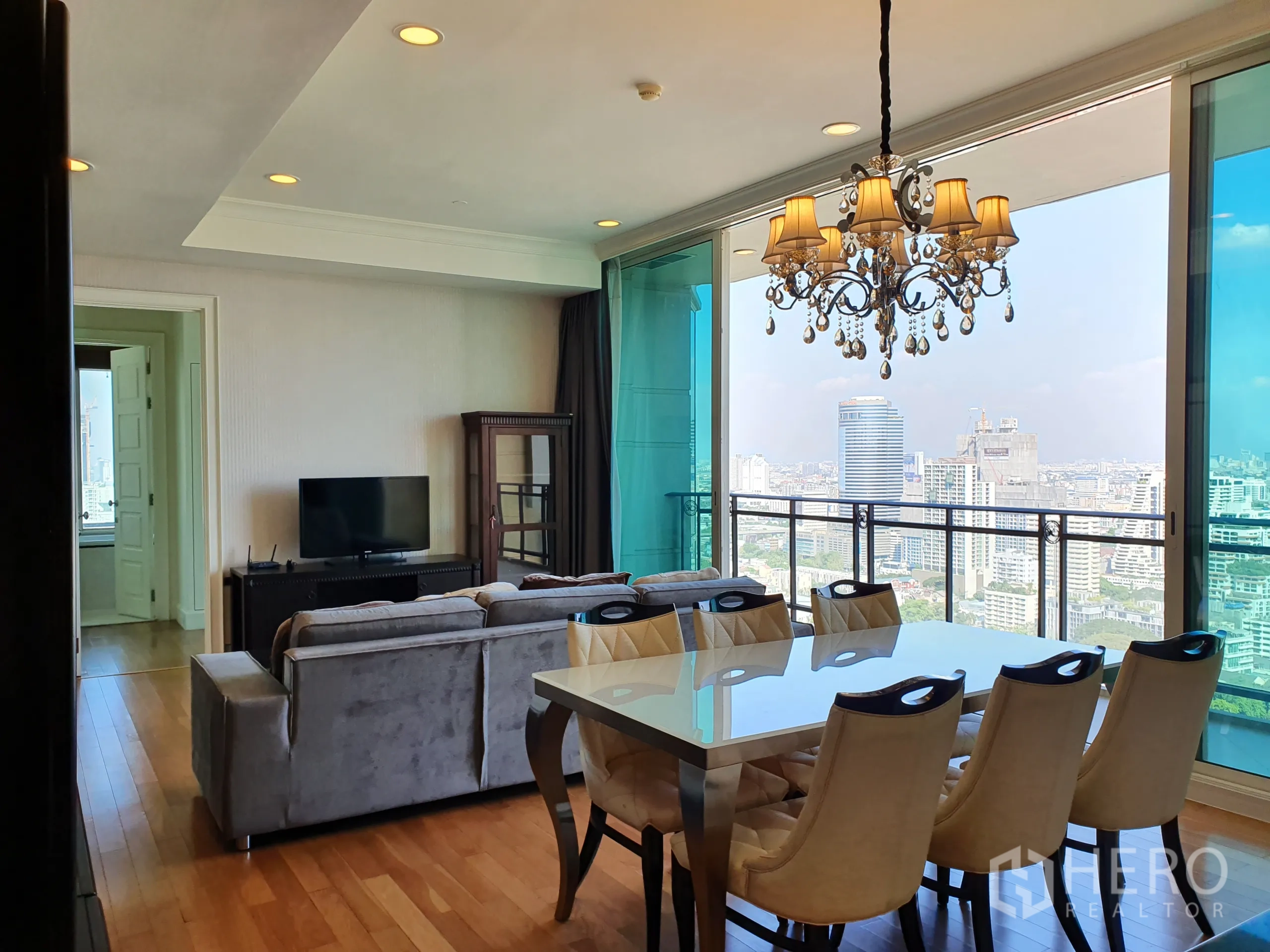 公寓 出租在Watthana, Bangkok - 餐区配水晶吊灯，紧邻大面窗与阳台，连接电视角，尽享城市景观。