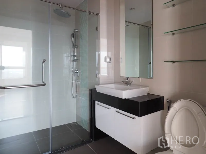 Condominium for rent in Yan Nawa, Bangkok - Modern bathroom with a glass shower enclosure, rain shower and floating vanity with mirror.