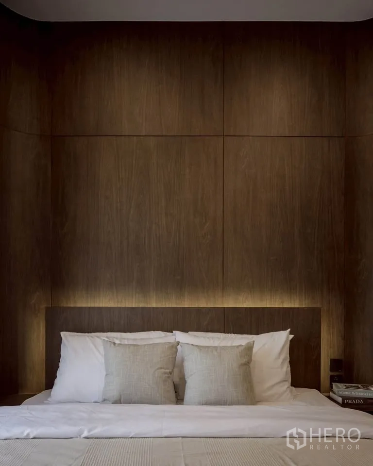 Condominium for rent in Khlong Toei, Bangkok - Bedroom with dark wood accent wall, backlit headboard, and pillows on bed.