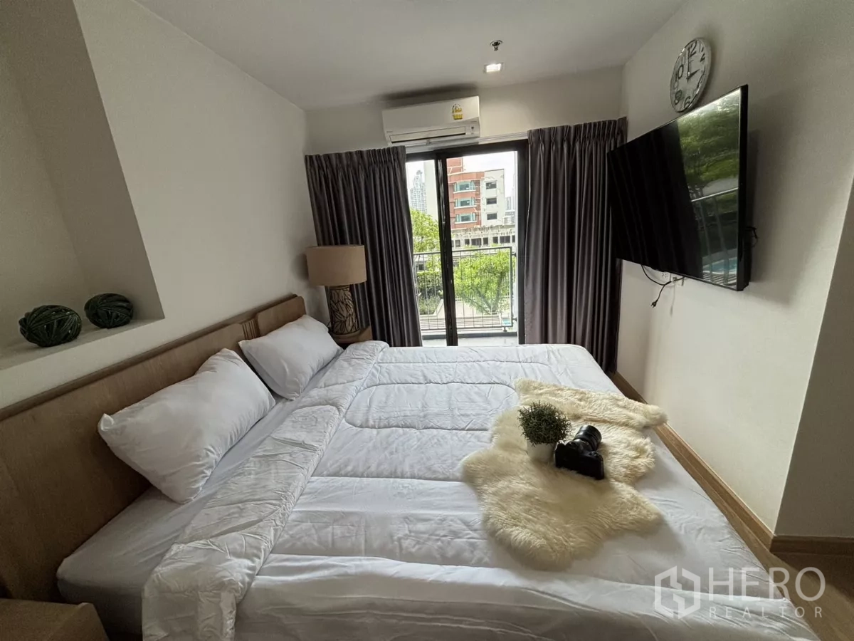 Condominium for rent in Phra Khanong, Bangkok - Master bedroom angle with wall-mounted TV and sliding doors to the balcony.