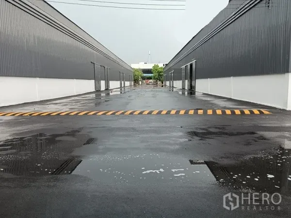 货栈 出租在Khlong Toei, Bangkok - 雨后两侧仓库之间的宽阔车道，黄色减速带与排水沟可见