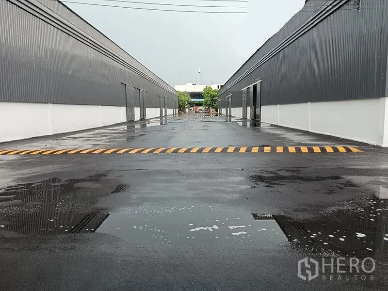 货栈 出租在Khlong Toei, Bangkok - 雨后两侧仓库之间的宽阔车道，黄色减速带与排水沟可见