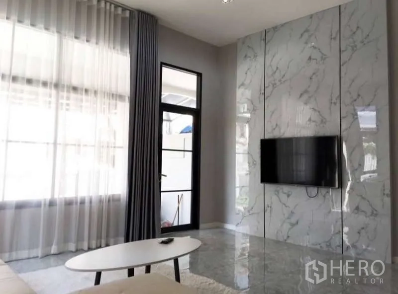 联排别墅 出租或出售在Prawet, Bangkok - 客厅电视背景墙为白色大理石板，旁有大窗与门