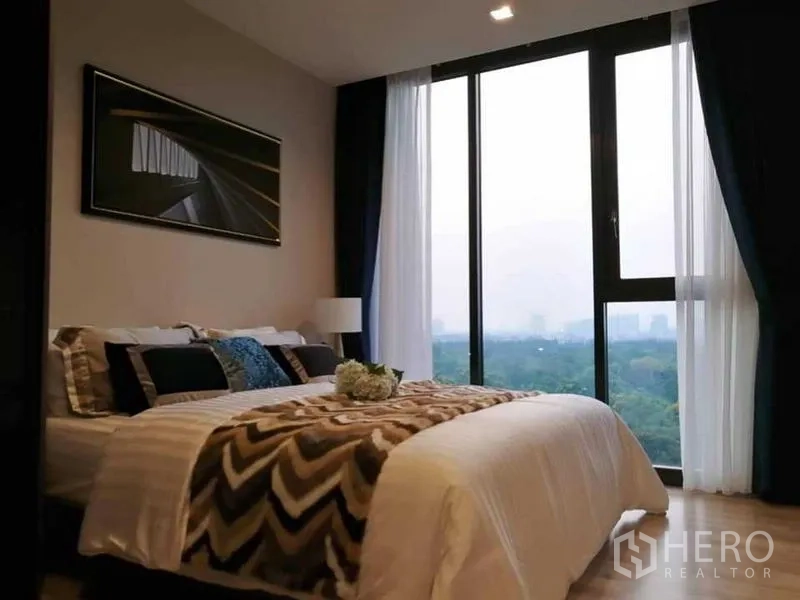 Condominium for rent in Chatuchak, Bangkok - Bedroom with floor-to-ceiling windows, sheer curtains and a wide green park view.