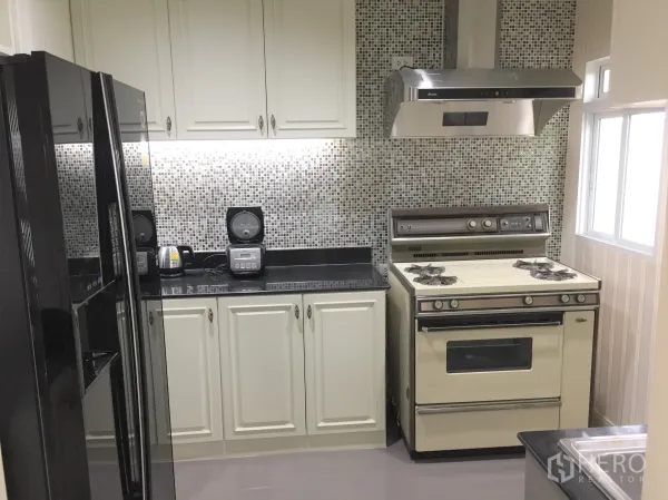 Detached House for rent in Saphan Sung, Bangkok - Fitted kitchen with mosaic backsplash, gas stove, range hood and a large black refrigerator.