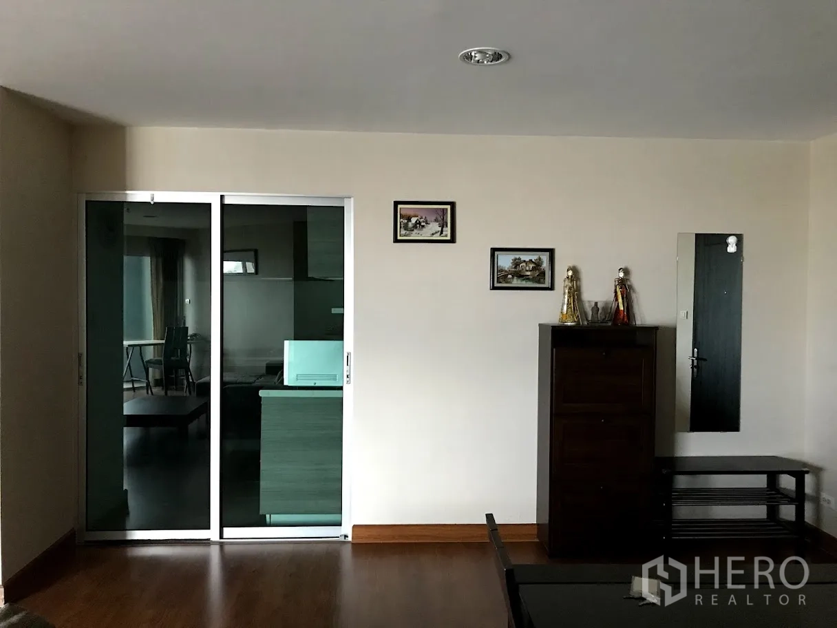 Condominium for rent in Huai Khwang, Bangkok - Living area wall with glass sliding door to the kitchen and a storage cabinet with decor.