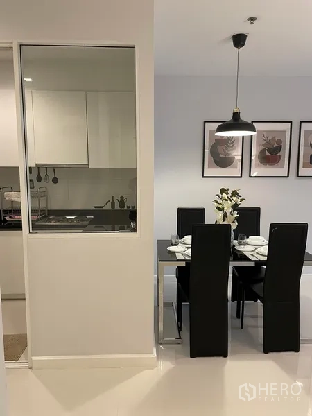 Condominium for rent or sale in Watthana, Bangkok - Dining area beside a glass-partitioned kitchen with pendant light and framed wall art.