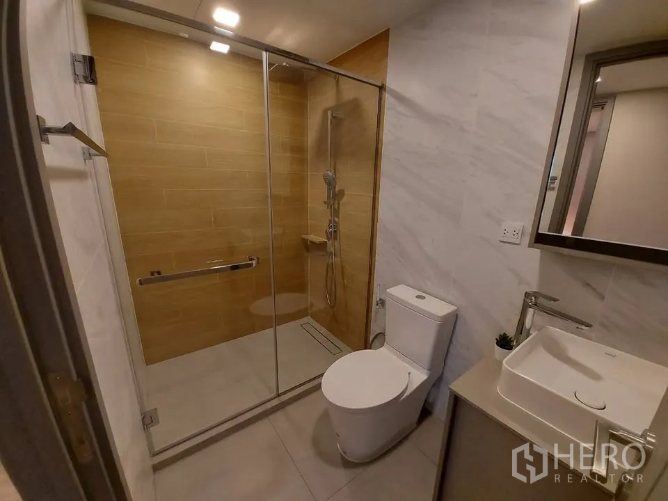 Condominium for rent in Watthana, Bangkok - Modern bathroom with glass shower, toilet and vanity on marble-look walls.