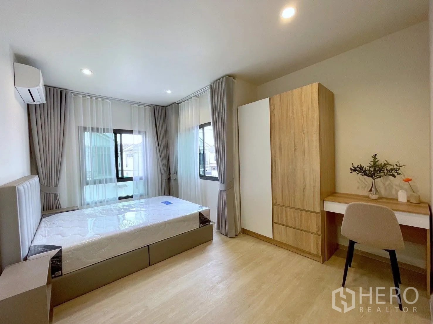 Detached House for rent in Bang Phli, Samut Prakan - Spacious bedroom with two windows, upholstered bed, wardrobe and study desk, light wood flooring.
