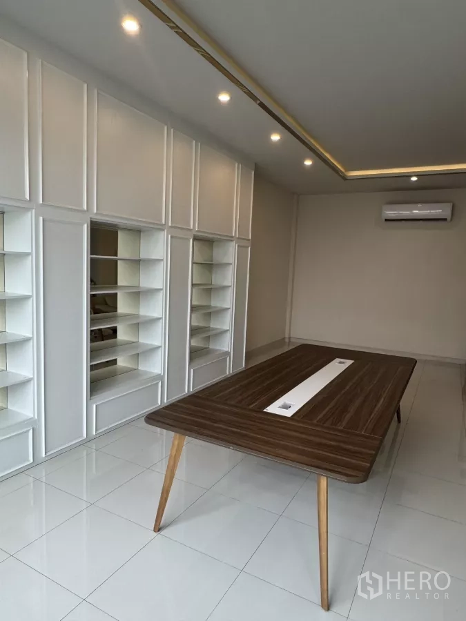 Factory for sale in Lam Luk Ka, Pathum Thani - Bright office with built-in shelving, recessed ceiling lights and a wooden meeting table on glossy tiles.