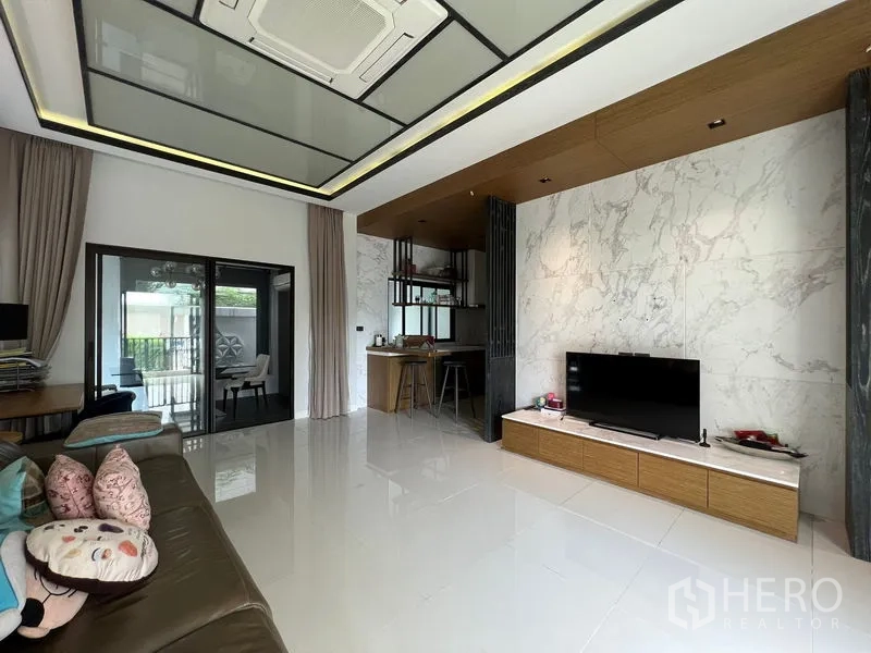 联排别墅 出租在Saphan Sung, Bangkok - 客厅一角，岩板纹理电视墙与厨房相邻。