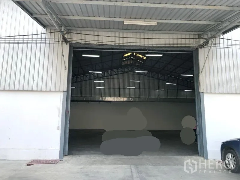 Warehouse for rent in Pak Kret, Nonthaburi - Wide entry with metal canopy and tall sliding doors opening to a well-lit warehouse space and loading area.