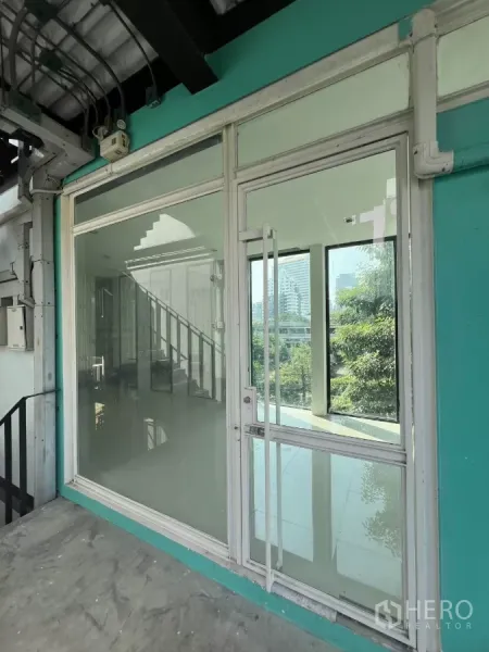 พื้นที่ขายปลีก ให้เช่าในWatthana, Bangkok - หน้าร้านกระจกชั้น 3 ผนังสีเทอร์คอยซ์ พร้อมทางขึ้นบันไดและวิวต้นไม้ด้านนอก