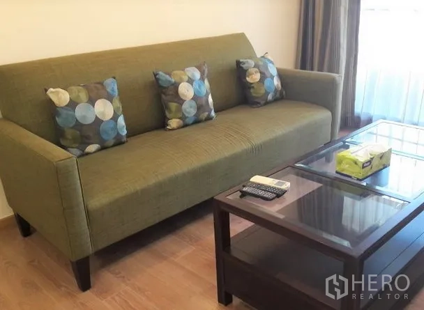 คอนโด ให้เช่าในPathum Wan, Bangkok - โซฟาสีเขียวพร้อมหมอนลายจุด ข้างโต๊ะกลางท็อปกระจก