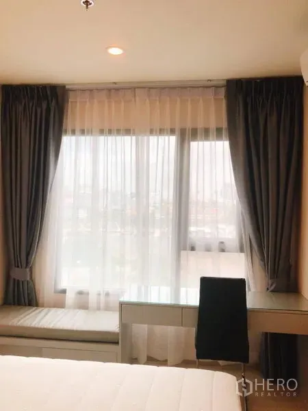 Condominium for rent in Huai Khwang, Bangkok - Bedroom with large windows, sheer curtains, writing desk and window seat.