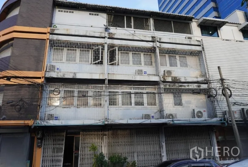 อาคารพาณิชย์ ให้เช่าในKhlong Toei, Bangkok - อาคารพาณิชย์หลายชั้นด้านหน้าอาคาร มีลูกกรงหน้าต่าง สีซีดจาง และคอมเพรสเซอร์แอร์ภายนอกในบรรยากาศเมืองกรุงเทพฯ