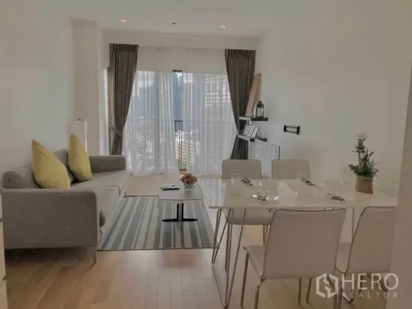 คอนโด ให้เช่าในBangkok - ห้องนั่งเล่นหันสู่หน้าต่างบานใหญ่ ผ้าม่านโปร่ง โซฟาสีเทา และโต๊ะทานอาหาร