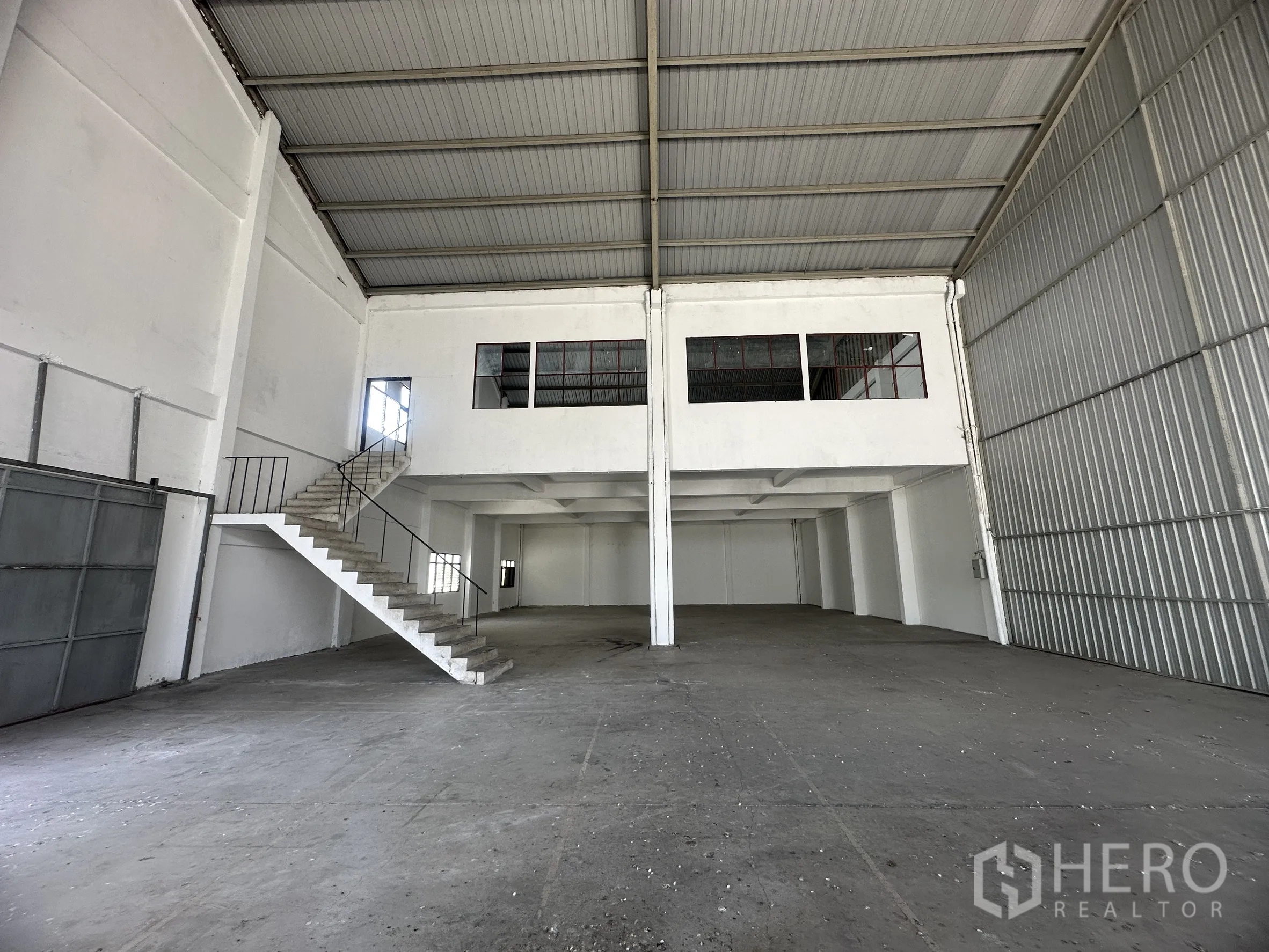 Factory for rent in Mueang Samut Prakan, Samut Prakan - Clear-span factory floor beneath a high roof with mezzanine offices and stair access.