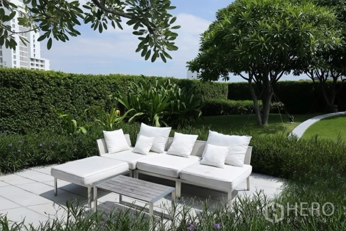 Condominium for rent in Watthana, Bangkok - Shaded garden lounge with white outdoor sofa surrounded by lush hedges and trees.