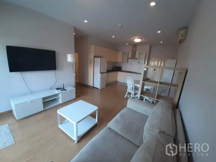 Condominium for sale in Wang Thonglang, Bangkok - Living room with sofa, wall-mounted TV and modern open kitchen.