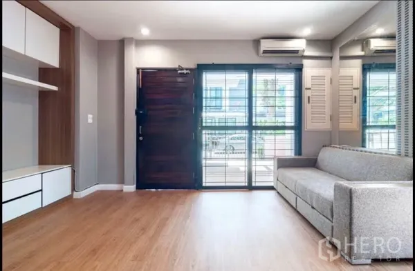 ทาวน์เฮาส์ ขายในKhlong Toei, Bangkok - ห้องนั่งเล่นสว่างพื้นไม้ หน้าต่างบานใหญ่ มีเครื่องปรับอากาศและโซฟาสีเทาใกล้ประตูเข้า