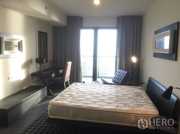 Condominium for rent or sale in Bang Lamung, Chon Buri - Bright bedroom with bed, work desk and floor-to-ceiling windows opening to a balcony.