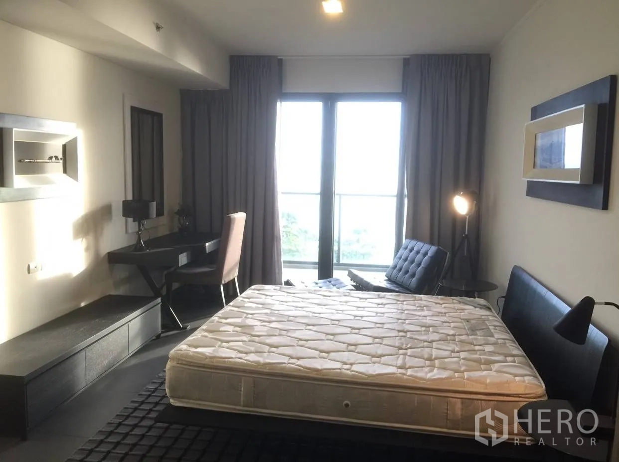 Condominium for rent or sale in Bang Lamung, Chon Buri - Bright bedroom with bed, work desk and floor-to-ceiling windows opening to a balcony.