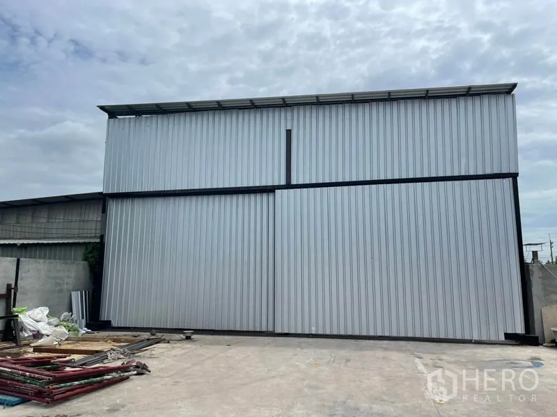 货栈 出租或出售在Khlong Luang, Pathum Thani - 金属板外墙的仓库正面，高大推拉门，前方宽阔的混凝土场地。