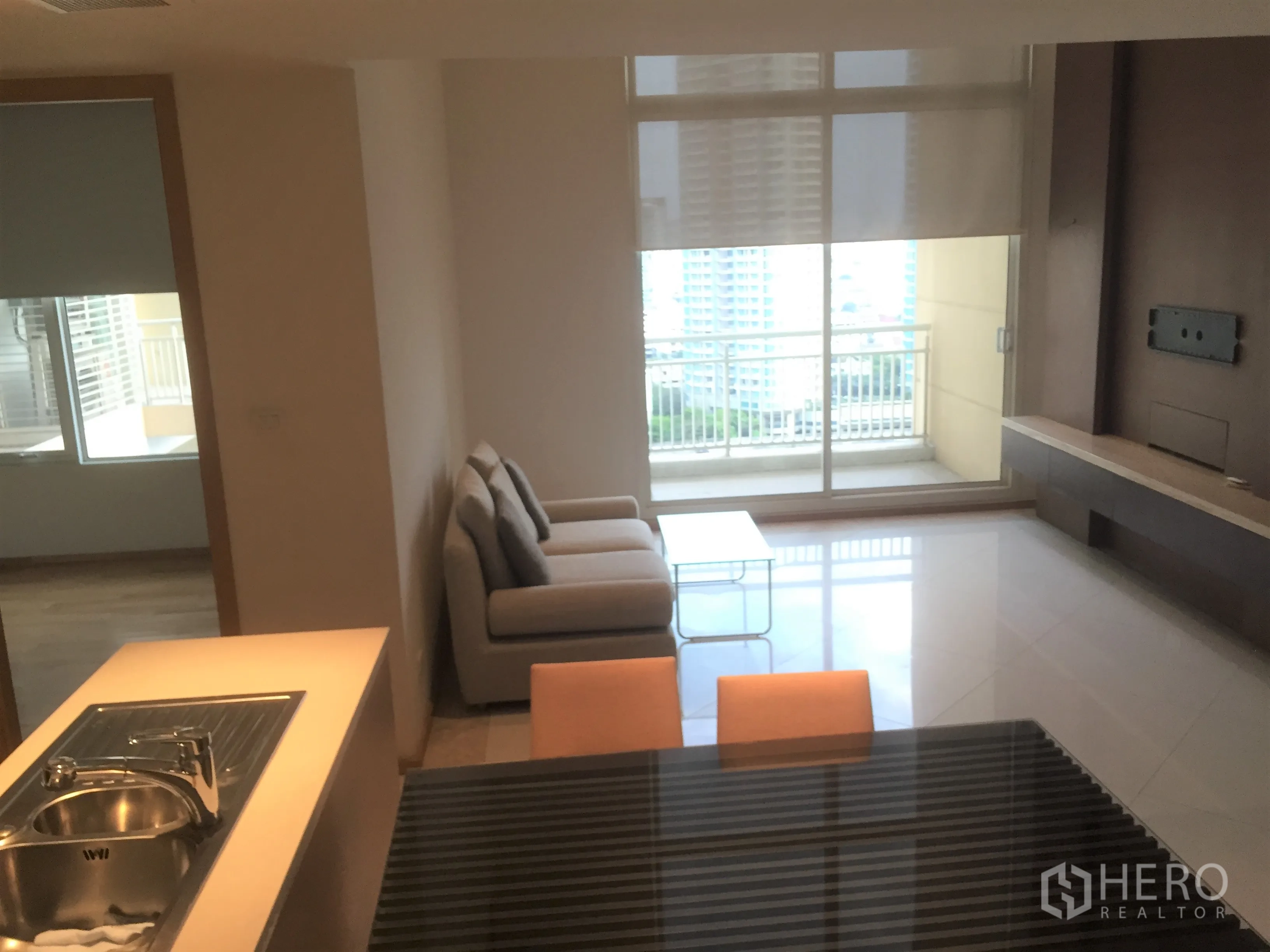 Condominium for rent in Sathon, Bangkok - Bright living room with sofa, built-in TV wall and sliding doors opening to a balcony with city view.