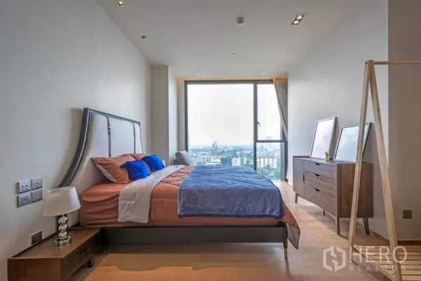 公寓 出租在Khlong Toei, Bangkok - 明亮的一居室卧室，落地窗与城市天际线景观，木地板与现代家具。