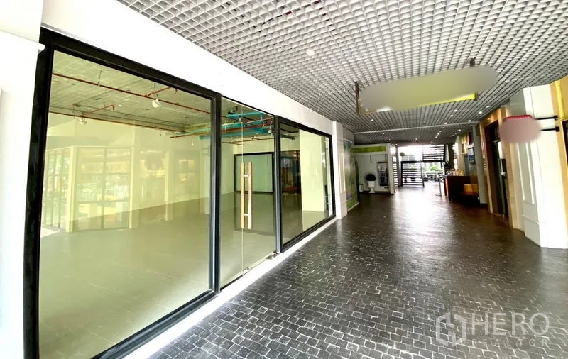 พื้นที่ขายปลีก ให้เช่าในKhlong Toei, Bangkok - หน้าร้านกระจกสูงจรดเพดานติดกับโถงอาคาร ทางเดินพื้นสีดำและฝ้าเพดานลายตาราง