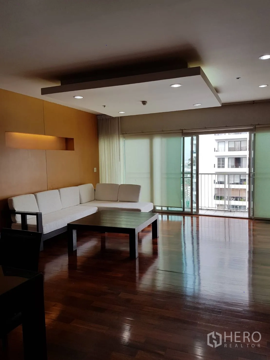 Condominium for rent or sale in Watthana, Bangkok - Spacious living room with L-shaped sofa, recessed lighting, and balcony access.