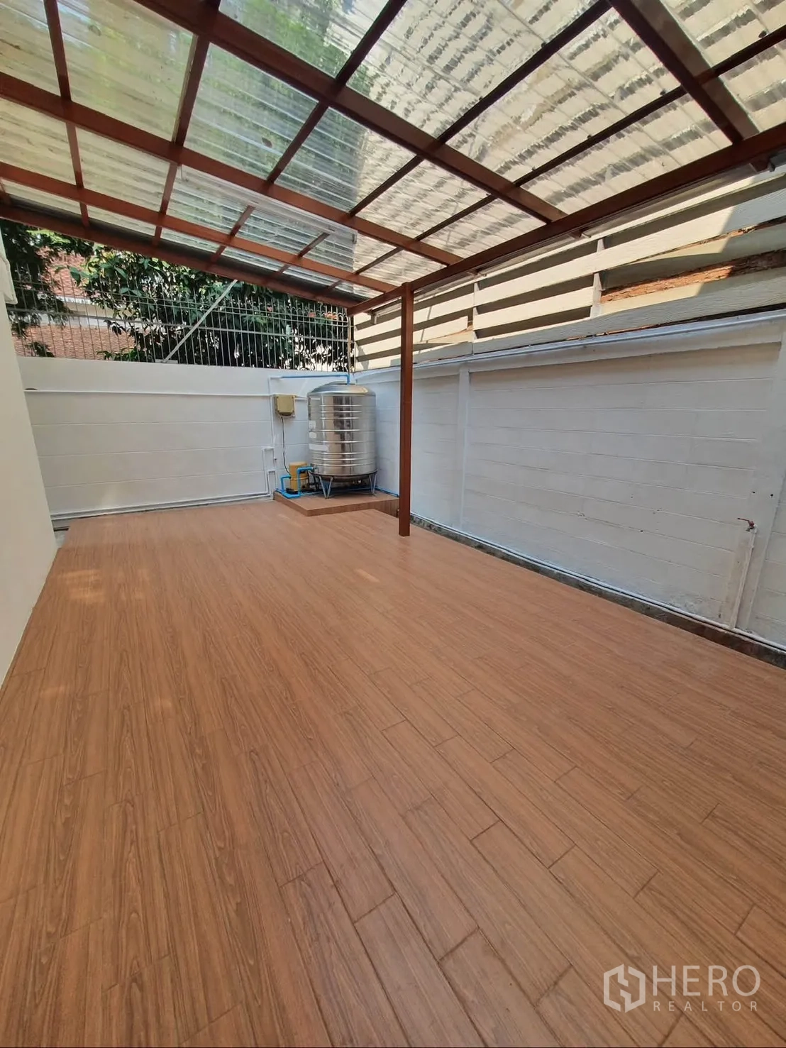 Detached House for rent in Sathon, Bangkok - Covered patio with wood-look flooring and a clear roof next to a stainless water tank.