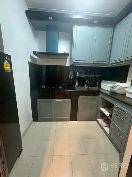 Townhouse for rent in Chom Thong, Bangkok - Compact kitchen with grey built-in cabinets, black backsplash, hob and hood.