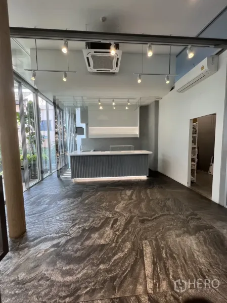 零售空间 出租在Khlong Toei, Bangkok - 明亮的店铺内景，带内置吧台、轨道灯、嵌入式空调与石纹地面，临整面落地玻璃。