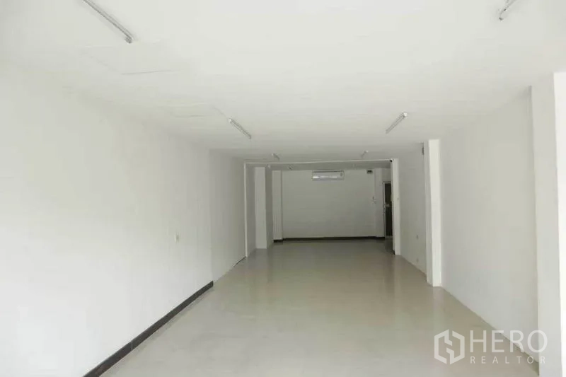 零售空间 出租在Watthana, Bangkok - 狭长店铺空间，白墙瓷砖地，天花灯带，后方设有空调。