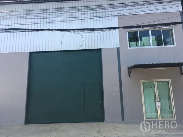 货栈 出租在Bang Kapi, Bangkok - 仓库外立面，超高绿色卷闸装货门与玻璃门办公室入口。