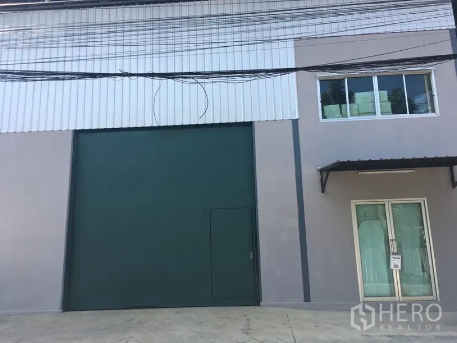 คลังสินค้า ให้เช่าในBang Kapi, Bangkok - ด้านหน้าโกดังสมัยใหม่พร้อมประตูม้วนสีเขียวขนาดใหญ่และทางเข้าออฟฟิศกระจก.