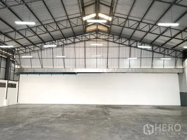 Warehouse for rent in Pak Kret, Nonthaburi - Spacious warehouse interior with high steel-truss roof, ridge skylights, LED lighting, and smooth concrete floor.