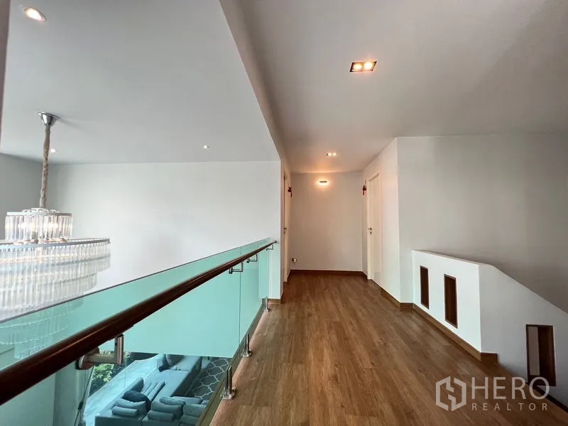 独立式住宅 出售在Chatuchak, Bangkok - 楼上走廊，木地板与玻璃栏杆，可俯瞰客厅及水晶吊灯。