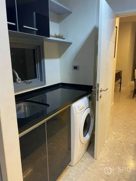 คอนโด ให้เช่าในKhlong Toei, Bangkok - ห้องเอนกประสงค์ เคาน์เตอร์ท็อปสีดำ อ่างล้างจาน และเครื่องซักผ้าฝาหน้าใกล้หน้าต่าง